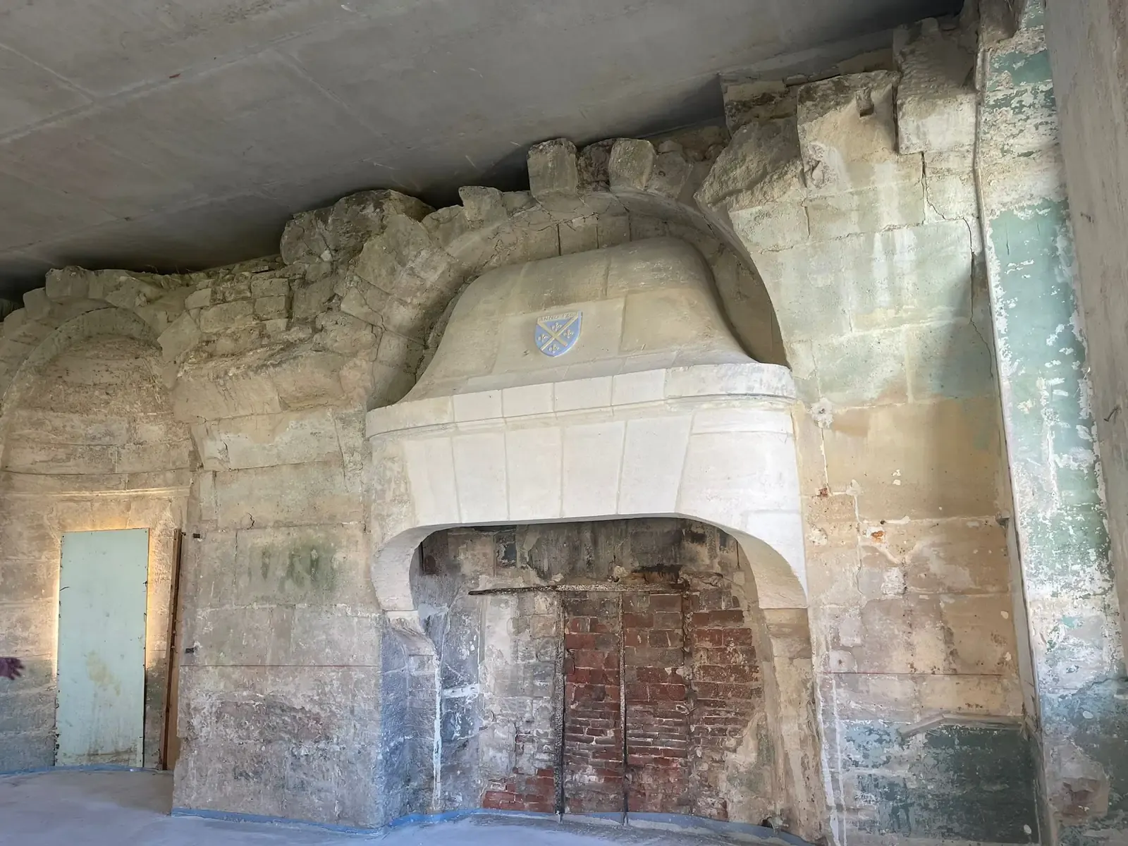 Salle du cabinet médical de Villers-sous-Saint-Leu avant travaux : murs de pierre et grande cheminée armoriée.
