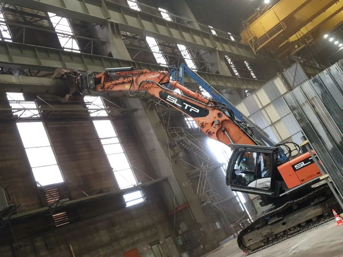 Pelle Hitachi orange siglée SLTP sous un pont roulant jaune, dans une halle de Framatome, au Creusot.