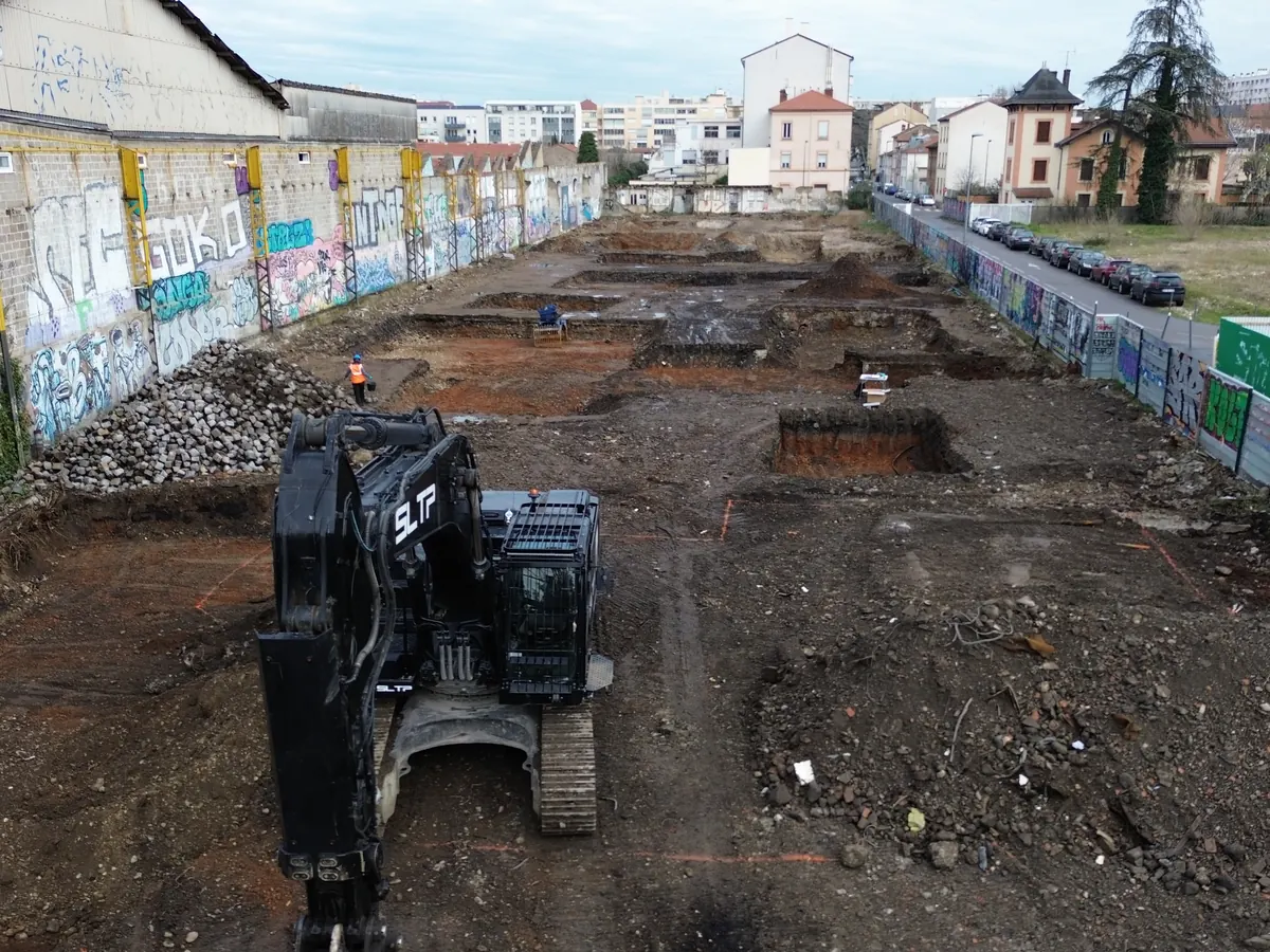 Vue au drone du chantier de dépollution Resor, à Villeurbanne : une pelle noire sur le terrain décapé.